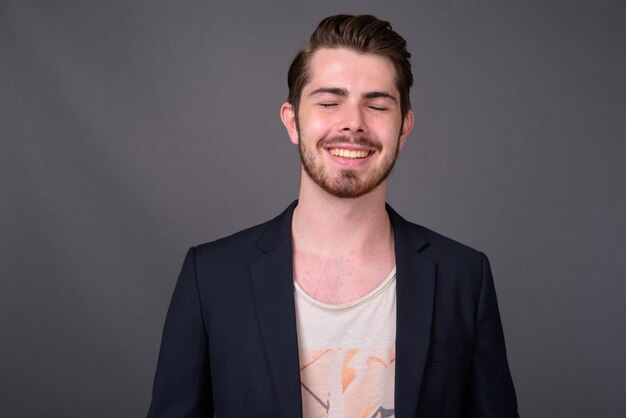 Young handsome bearded businessman against gray wall