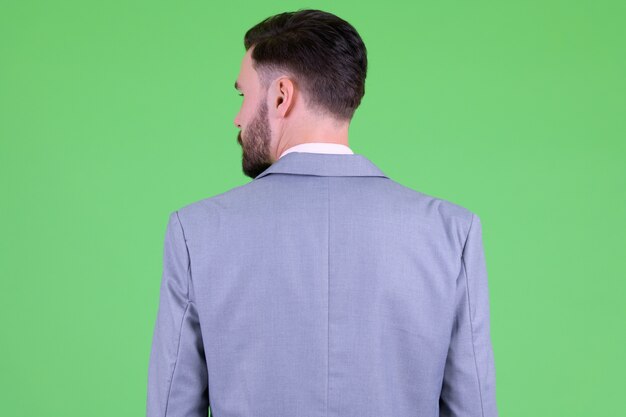  young handsome bearded businessman in suit against chroma key with green wall