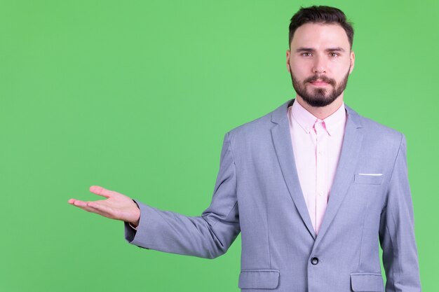  young handsome bearded businessman in suit against chroma key with green wall