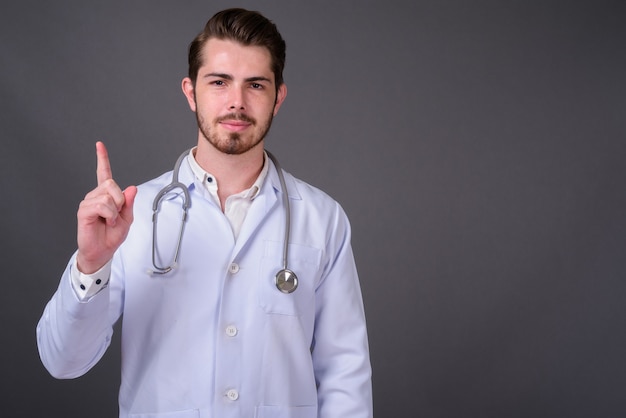 Young handsome bearded doctor against gray wall