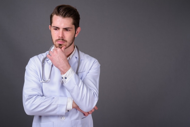 Young handsome bearded doctor against gray wall