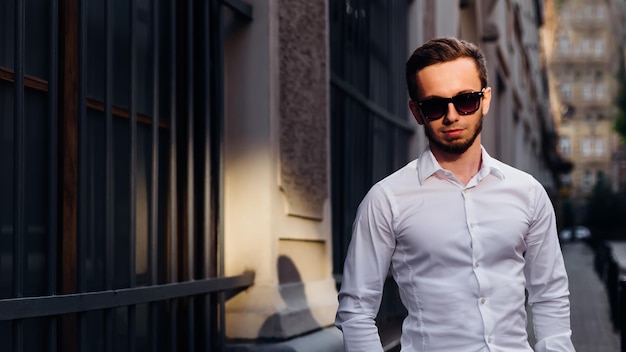 Giovane bel ragazzo barbuto che indossa una camicia bianca e occhiali da sole