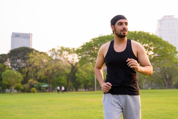 Young handsome bearded Indian man jogging at the park