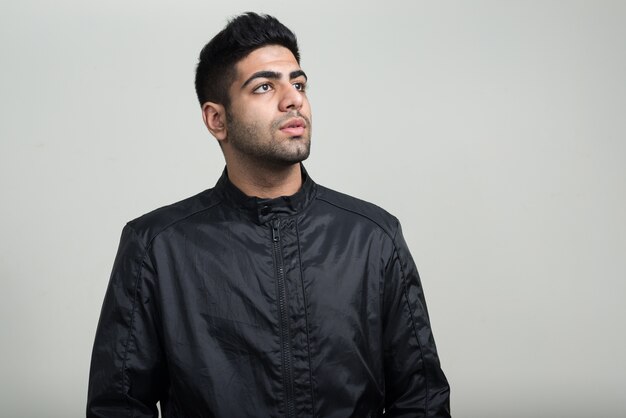 young handsome bearded Indian man with leather jacket as rock concept against white wall