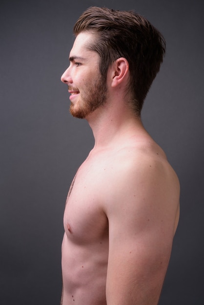 Young handsome bearded man shirtless against gray wall