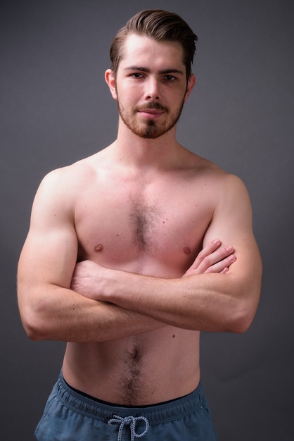 Young handsome bearded man shirtless against gray wall