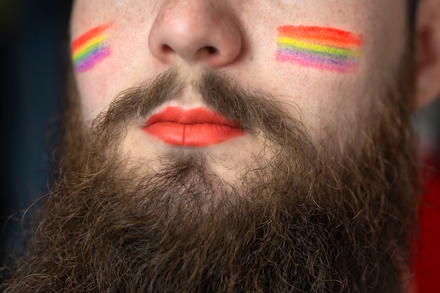 young handsome bearded man with pride flag on his cheek rainbow flag standing for lgbtq gender