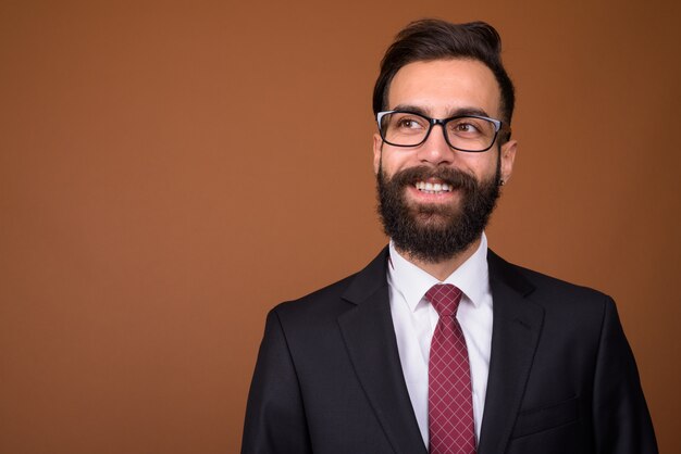 Young handsome bearded Persian businessman on brown wall