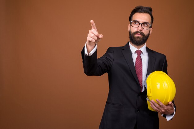 Young handsome bearded Persian businessman on brown wall