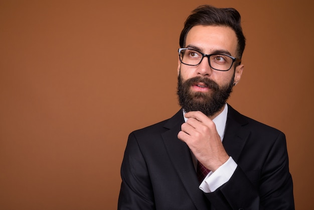 Young handsome bearded Persian businessman on brown wall