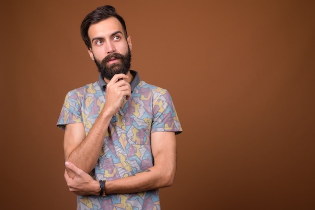 Young handsome bearded Persian man on brown wall