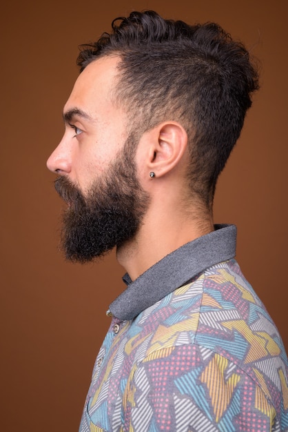 Молодой красивый бородатый персидский мужчина на коричневой стене