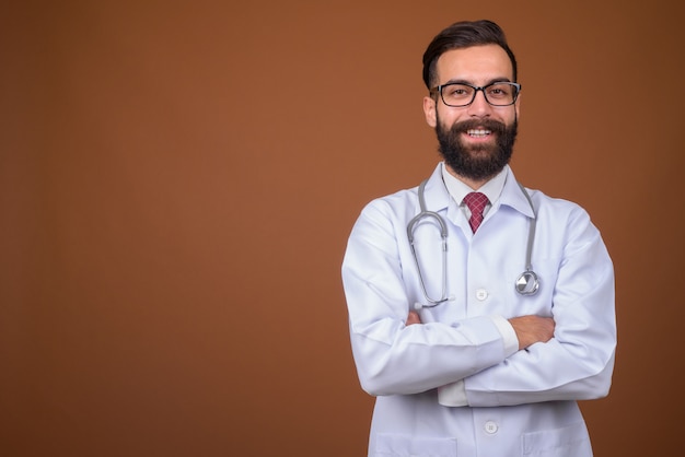 Young handsome bearded Persian man doctor on brown wall