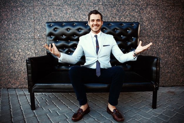 Young handsome bearded stylish man sitting on comfortable leather sofa outdoors.