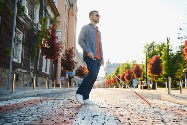 Photo young handsome blinded man walking with stick in town