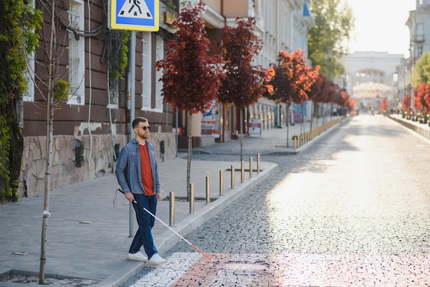 Молодой красивый ослепленный мужчина ходит с палкой по городу