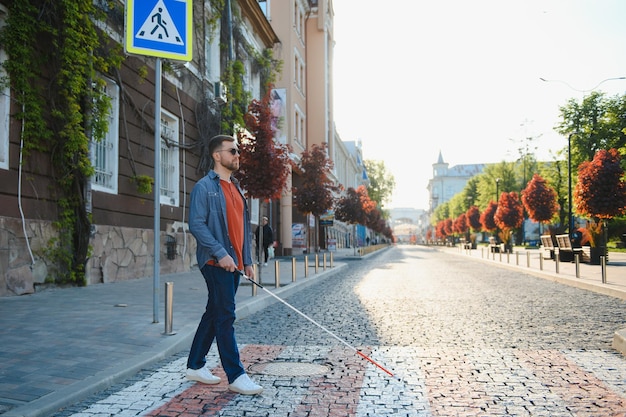 Young handsome blinded man walking with stick in town