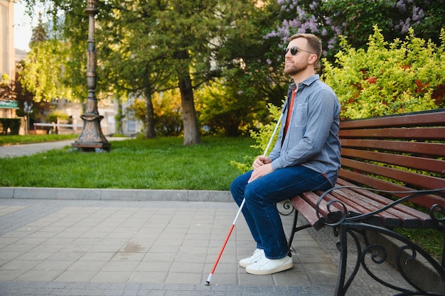 Young handsome blinded man walking with stick in town