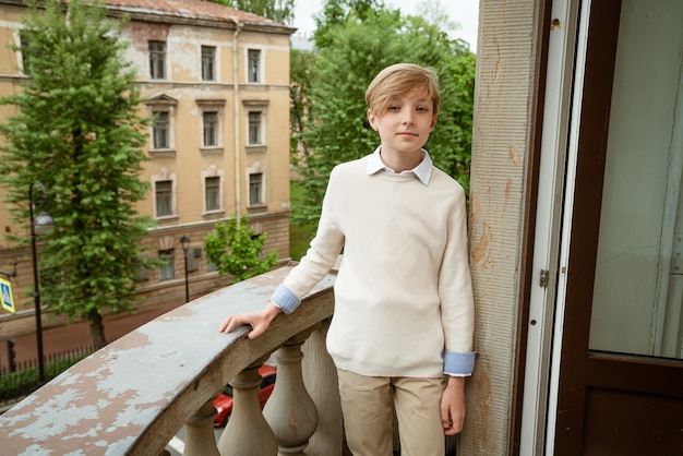 Молодой красивый блондин парень в бежевом свитере позирует на балконе