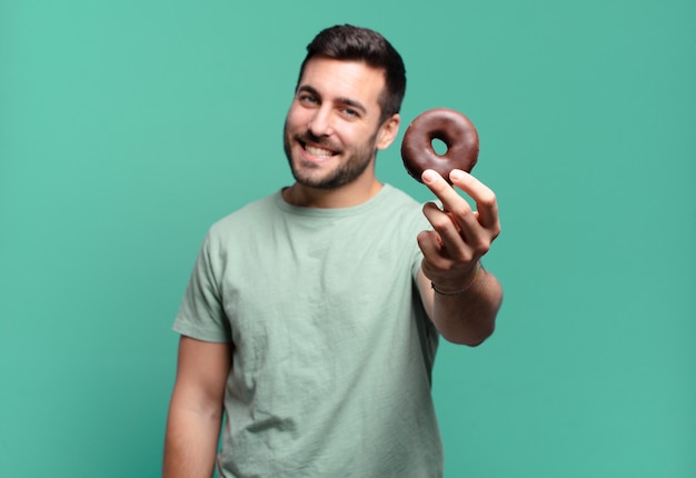 Giovane uomo biondo bello con una ciambella al cioccolato. concetto di colazione