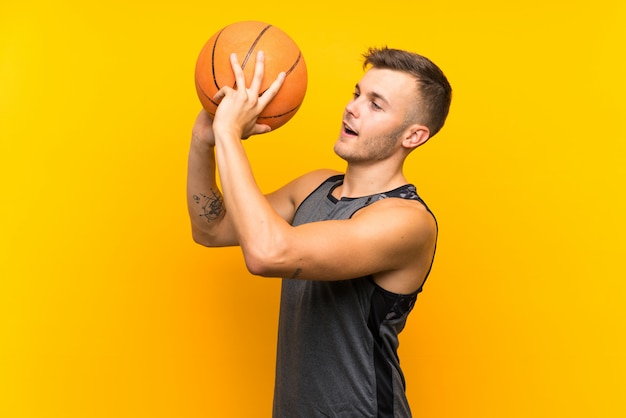 Young handsome blonde man holding a basket ball over isolated yellow wall
