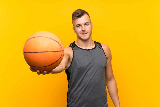 Young handsome blonde man holding a basket ball over isolated
yellow wall