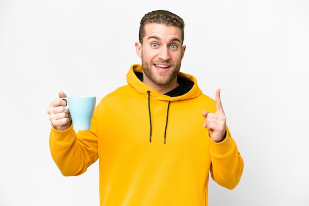 Young handsome blonde man holding cup of coffee over isolated background pointing up a great idea