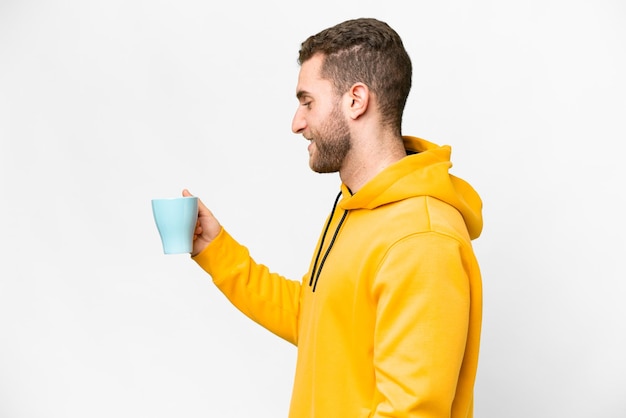 Young handsome blonde man holding cup of coffee over isolated background with happy expression