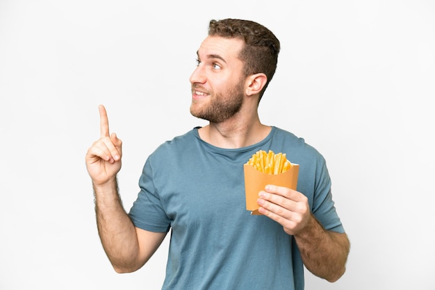 Young handsome blonde man holding fried chips over isolated white background pointing up a great idea