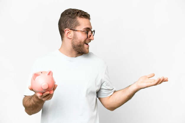 Young handsome blonde man holding a piggybank with surprise facial expression