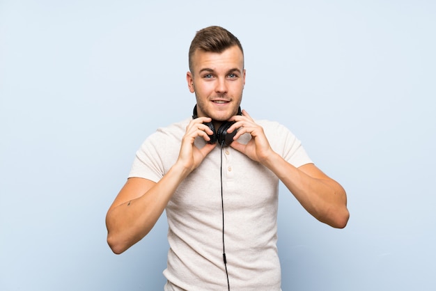 Young handsome blonde man over isolated blue wall listening to music with headphones