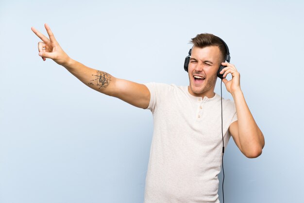 Young handsome blonde man over isolated blue wall listening to music with headphones