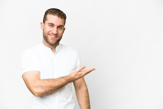 Young handsome blonde man over isolated white background presenting an idea while looking smiling towards