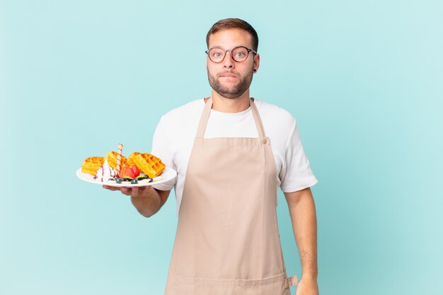 Giovane uomo biondo bello che sembra perplesso e confuso. cucinare il concetto di waffle