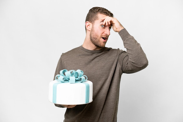 Young handsome blonde man with a big cake over isolated white background doing surprise gesture while looking to the side