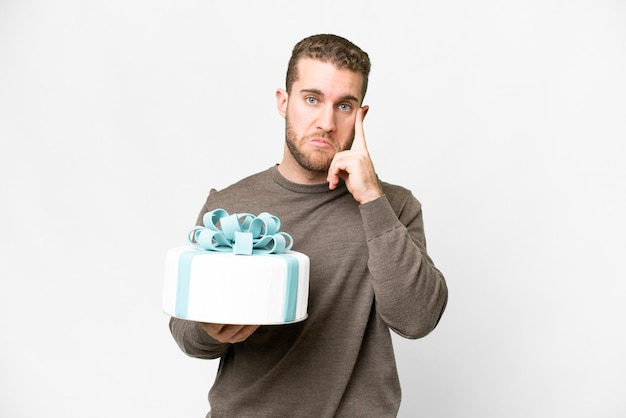 Young handsome blonde man with a big cake over isolated white background thinking an idea