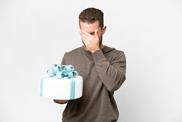 Young handsome blonde man with a big cake over isolated white background with tired and sick expression