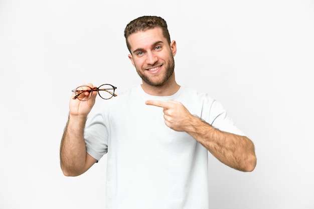 Young handsome blonde man with glasses over isolated white background and pointing it