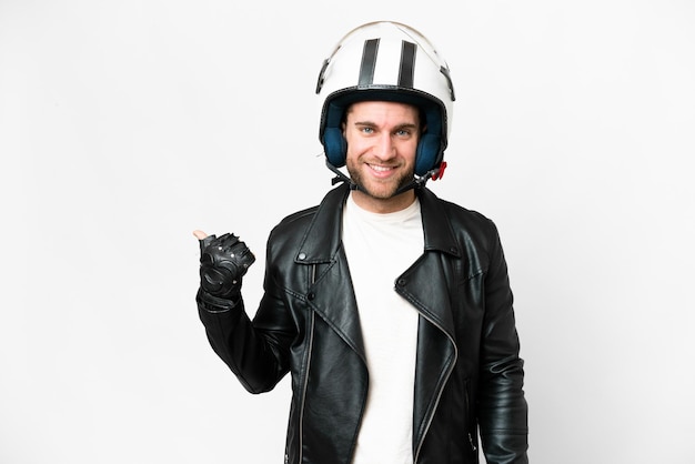 Young handsome blonde man with a motorcycle helmet over isolated white background pointing to the side to present a product