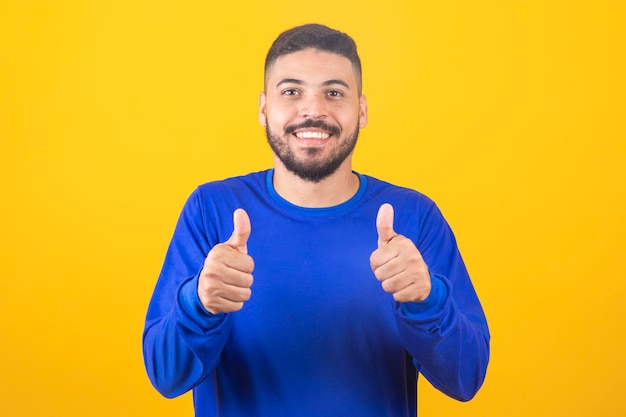 Young handsome boy on blue background showing thumbs up