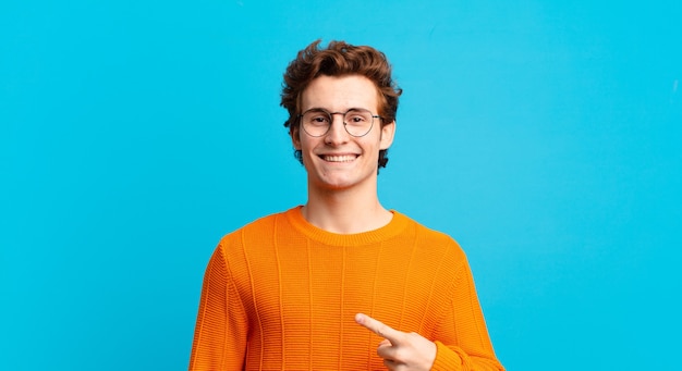 Young handsome boy smiling cheerfully, feeling happy and pointing to the side and upwards, showing object in copy space