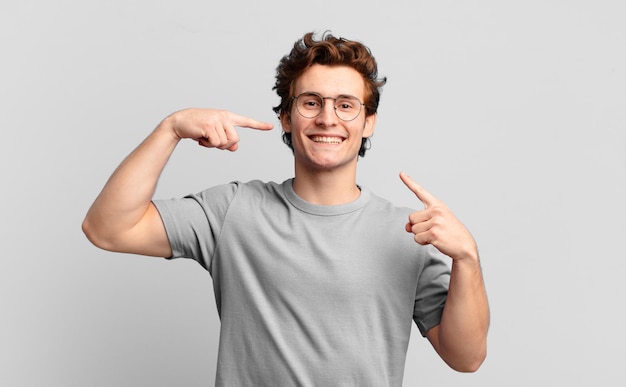 Young handsome boy smiling confidently pointing to own broad smile, positive, relaxed, satisfied attitude