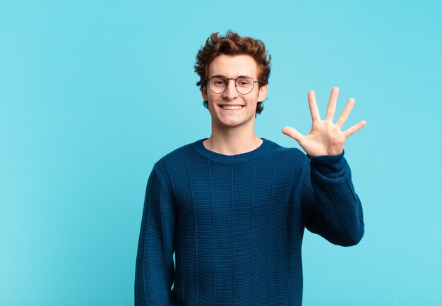 Young handsome boy smiling and looking friendly, showing number five or fifth with hand forward, counting down