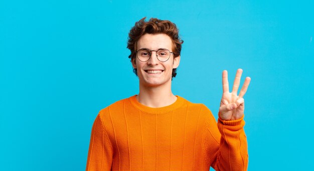 Young handsome boy smiling and looking friendly, showing number three or third with hand forward, counting down