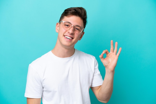 Young handsome Brazilian man isolated on blue background With glasses and doing OK sign