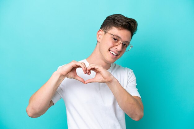 Young handsome Brazilian man isolated on blue background With glasses making heart with hands