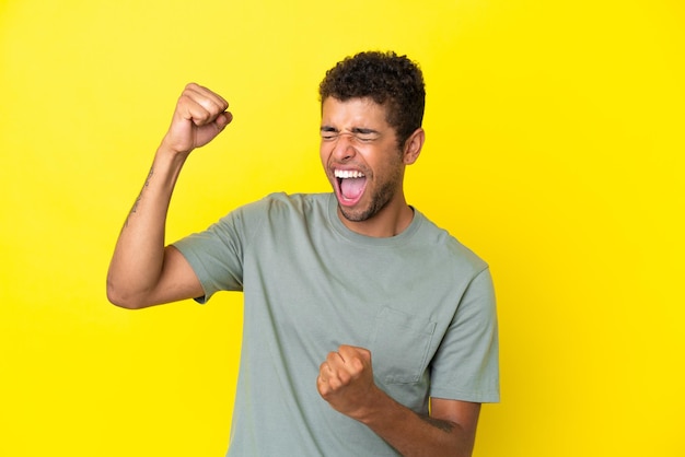 Young handsome brazilian man isolated on yellow background celebrating a victory