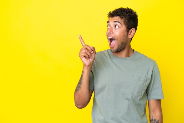 Young handsome Brazilian man isolated on yellow background intending to realizes the solution while lifting a finger up