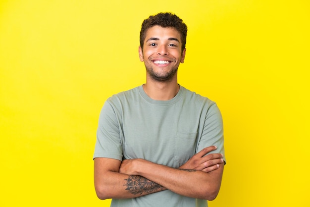 Young handsome Brazilian man isolated on yellow background keeping the arms crossed in frontal position