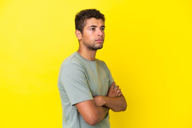 Young handsome Brazilian man isolated on yellow background looking to the side